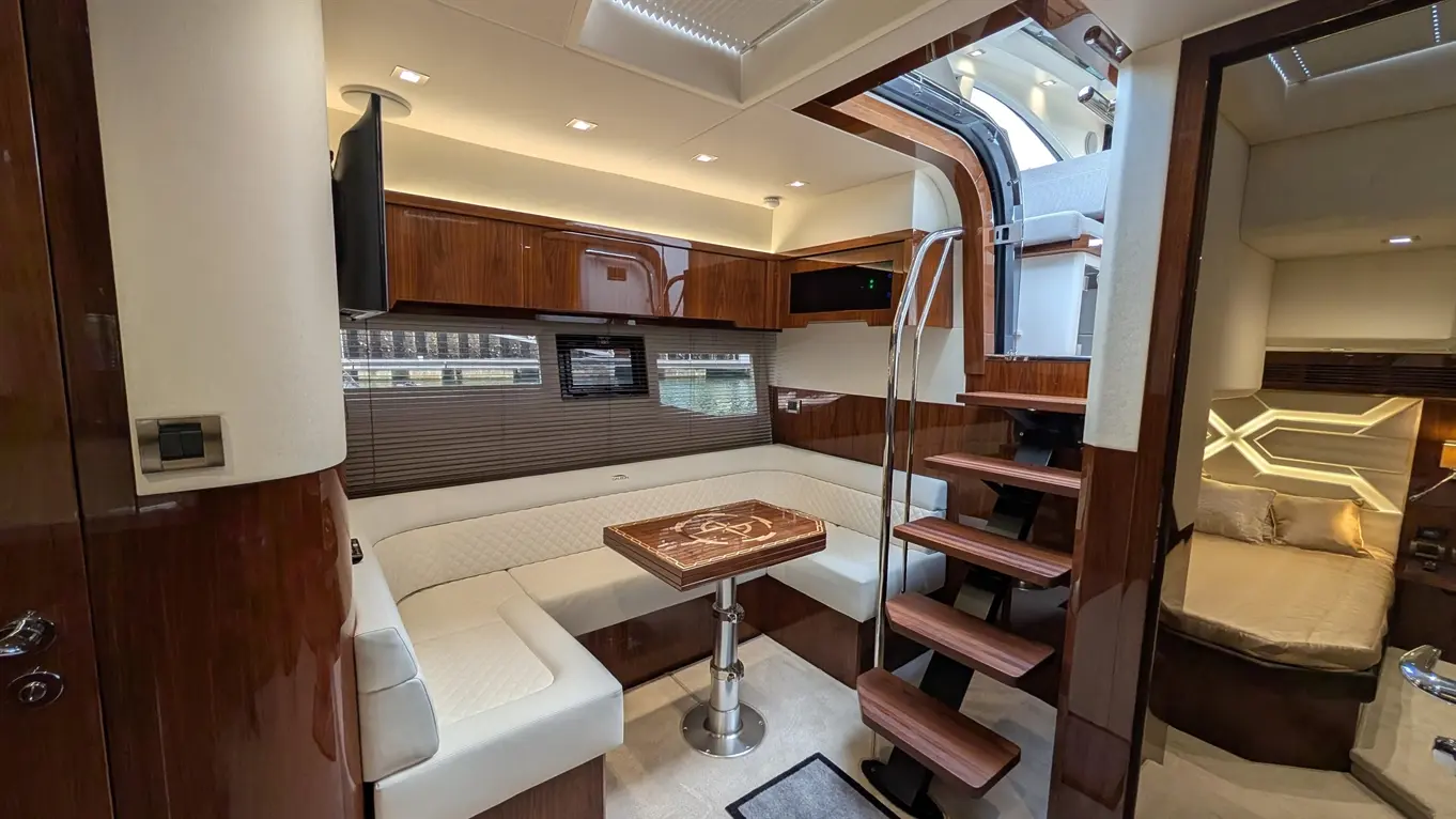 Luxurious boat interior featuring a seating area, wooden table, staircase, TV, and plush bedding in the cabin.